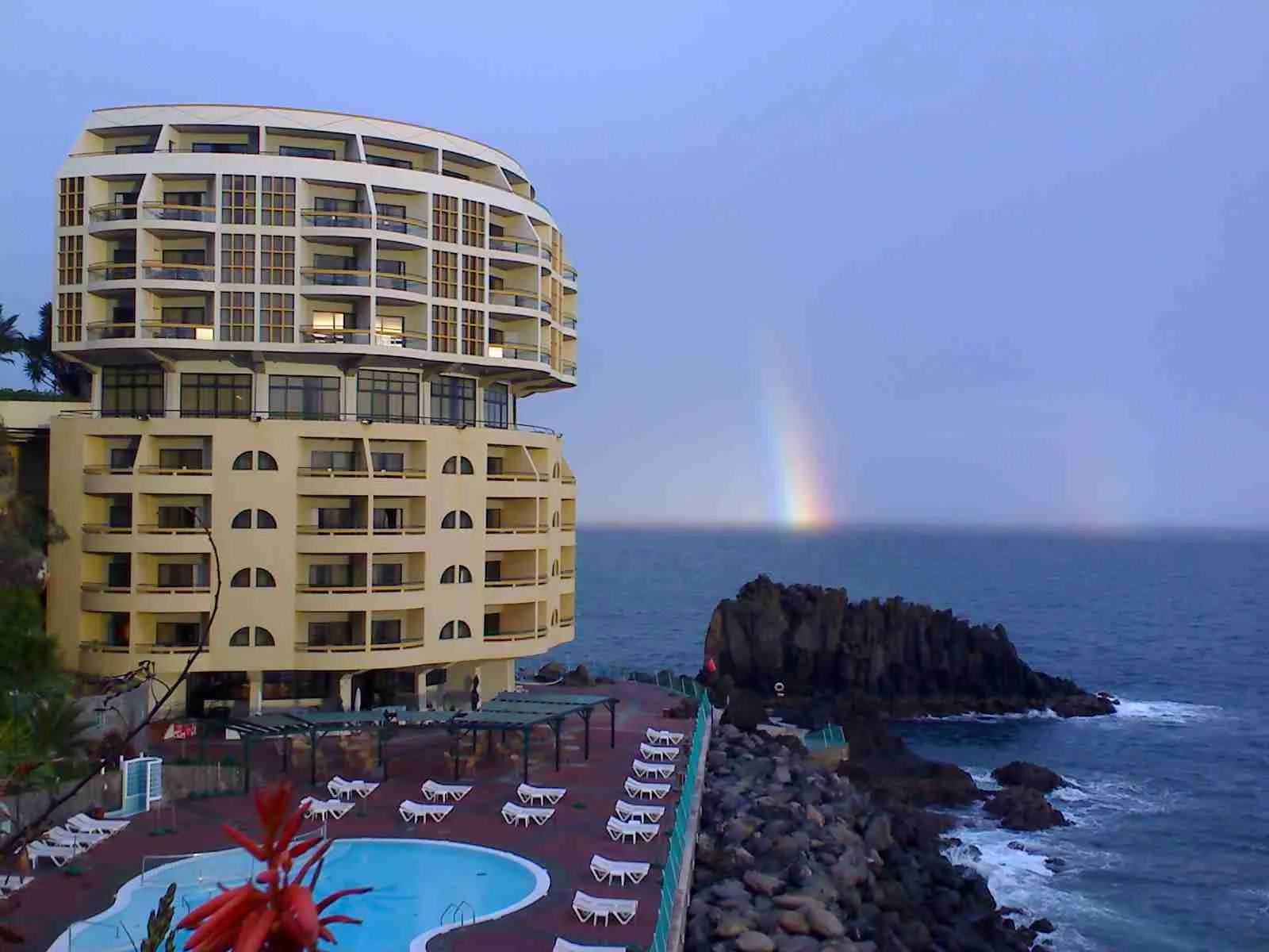 Hotel junto al mar y una piscina, con un arcoíris sobre el agua