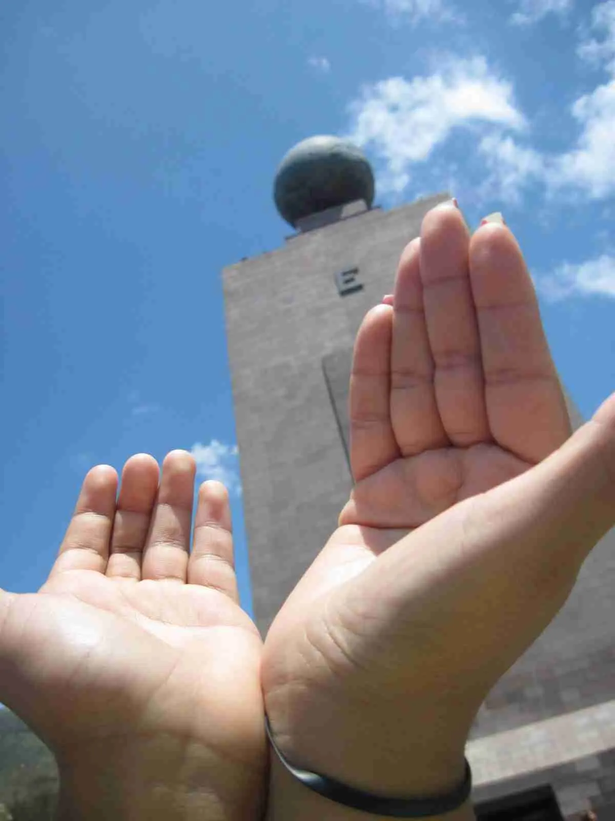 Dos manos abiertas delante del monumento de la Mitad del Mundo