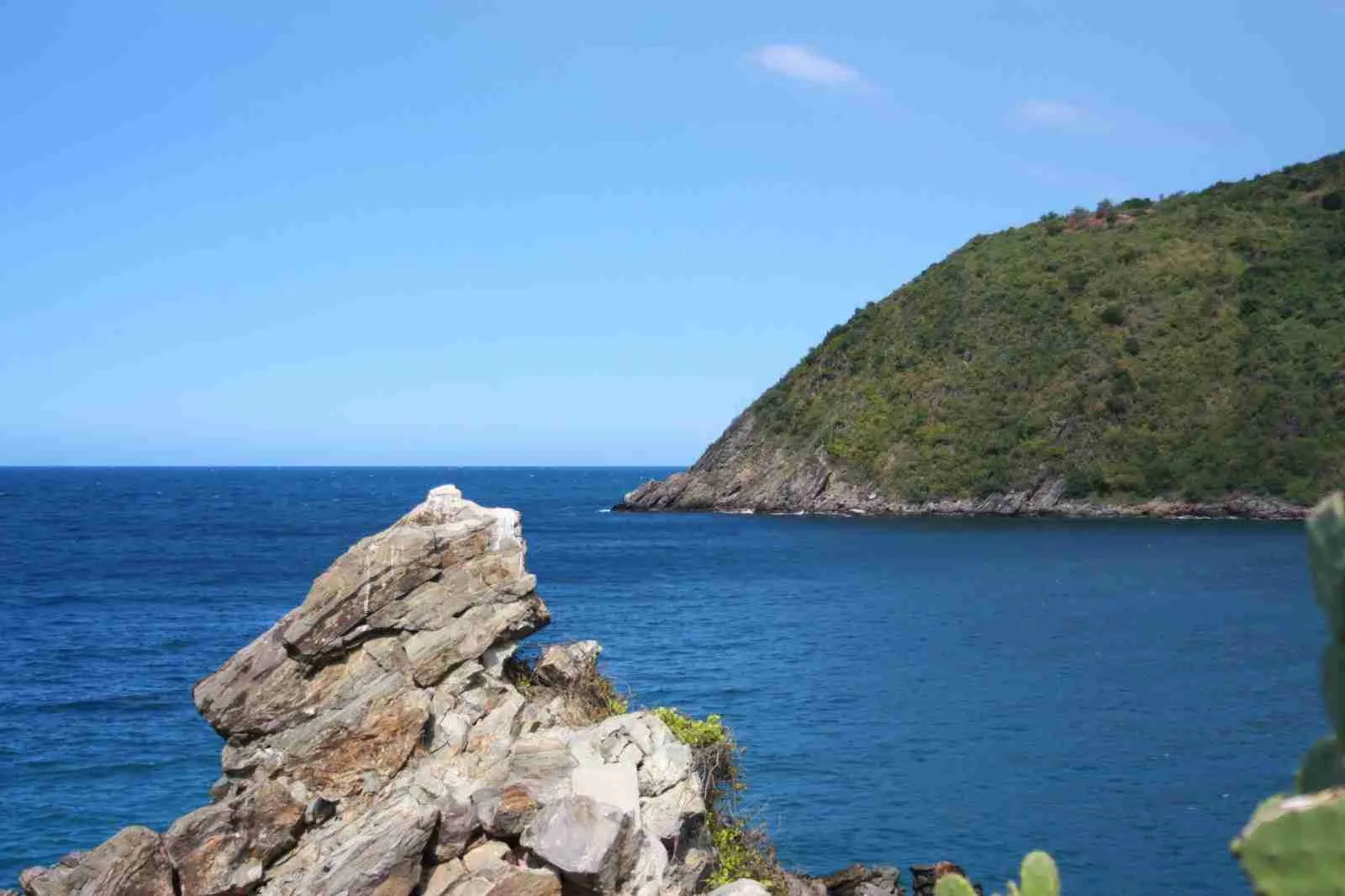 Roca junto al mar azul y un cerro cubierto de vegetación