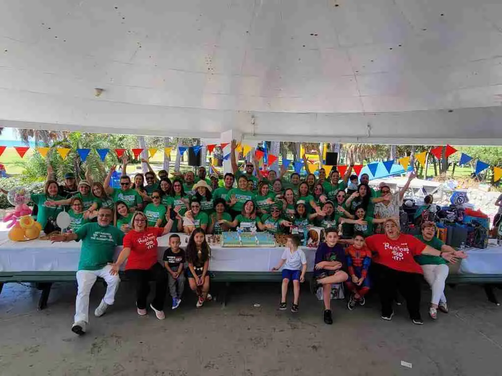 Grupo numeroso posando bajo una carpa decorada con banderines de colores, con niños sentados delante