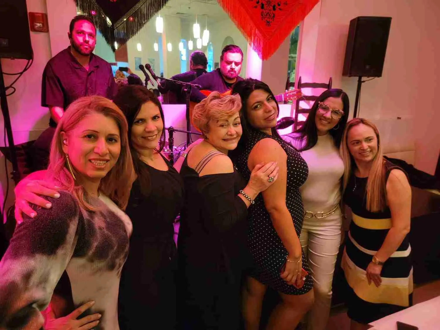 Grupo de mujeres posando delante de un escenario con músicos iluminado de rosa