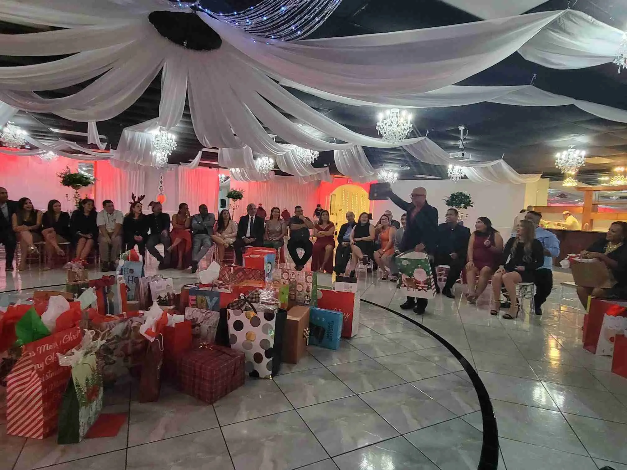 Salón de fiesta navideña con regalos en el suelo y los invitados sentados alrededor