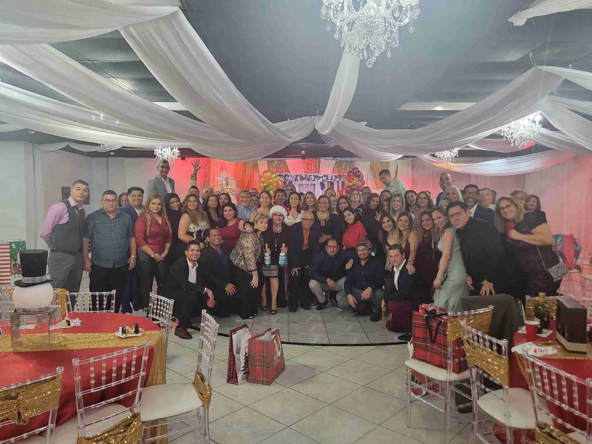 Foto de grupo en una fiesta navideña con mesas decoradas de rojo y dorado