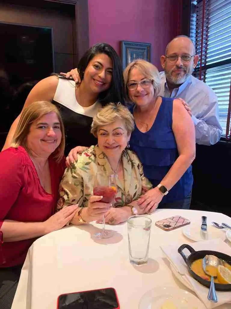 Cuatro personas sonriendo alrededor de una señora sentada a la mesa en un restaurante