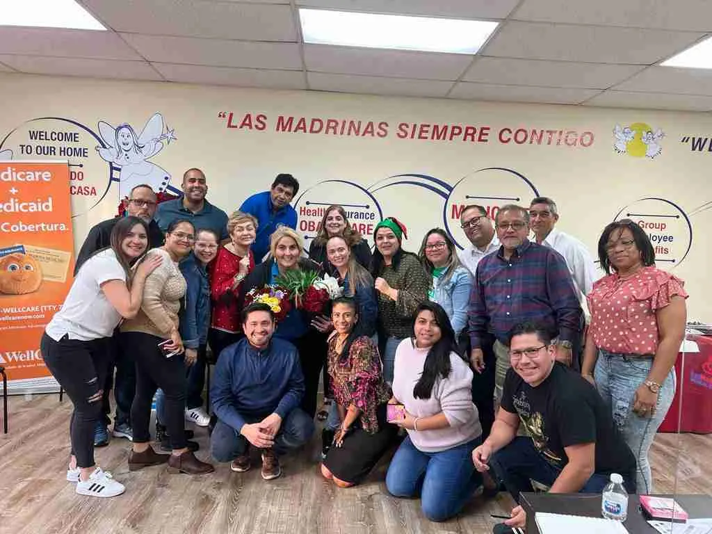 Equipo posando en una oficina con el lema Las Madrinas siempre contigo en la pared