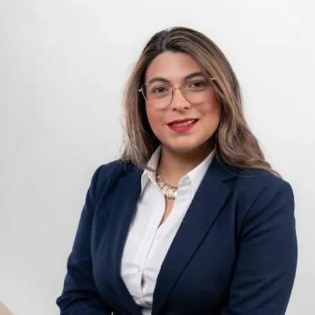 Retrato de Sharon Gómez Rivas sonriendo, con gafas y chaqueta azul marino
